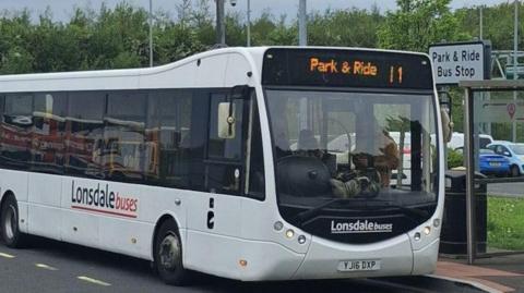 Large white bus with the words 'park and ride' in orange on the front of it.