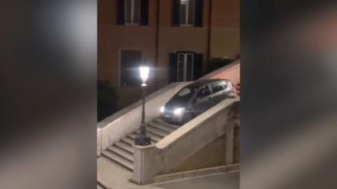 A grey car drives down the Spanish Steps at night with a street lamp illuminated next to it.