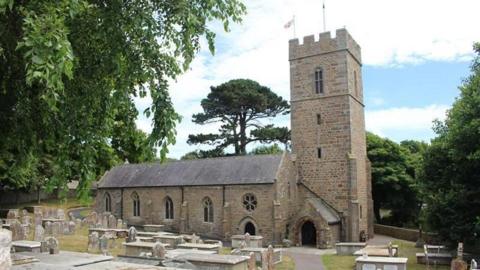 A church in a graveyard surrounded by trees and cloudy skies