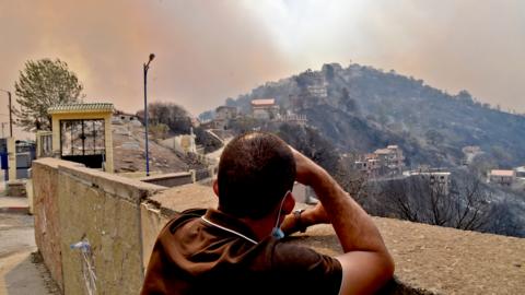 A man looks on as smoke rises from a wildfire in the forested hills of the Kabylie region, east of the capital Algiers, on August 10, 2021.