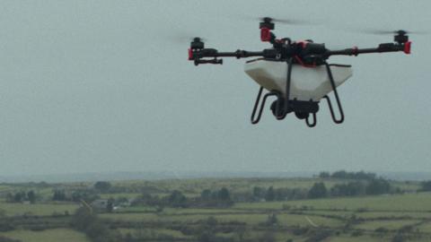 A drone with four rotors flies above the English countryside