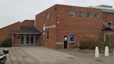 The entrance to The Swan Theatre, a brick building with a white image of a swan and "Swan Theatre" in white letters on one of the walls.