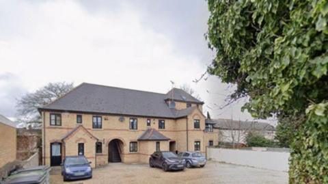 Henry Court is a modern redbrick building with an arched entrance and stairs leading to the upper floors. There are some cars parked at the front.