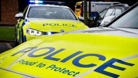 A stock picture of two Northumbria Police cars parked near a police van. The one in the foreground has Police: Proud to Protect in blue lettering on the yellow background