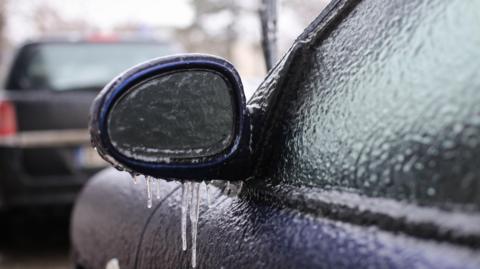 image of the side of a car and wingmirror covered in ice.