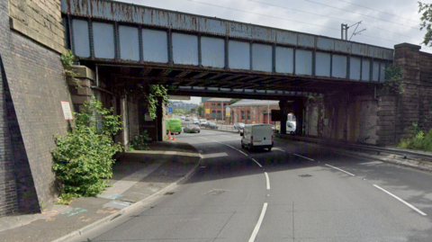 A three-lane road leading under a pair of railway bridges