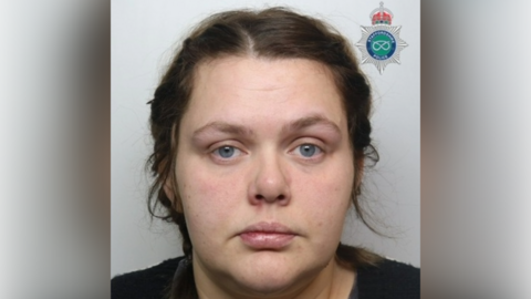A mugshot of a woman with brown hair and wearing a dark top.