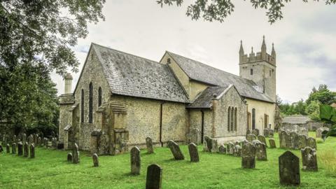 A large grey stone church and grassy graveayard