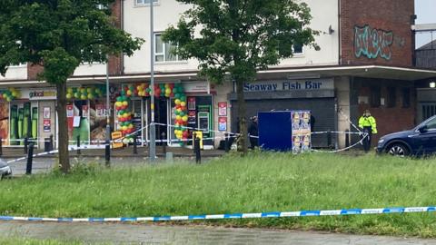 Police tape outside shops in Shard End