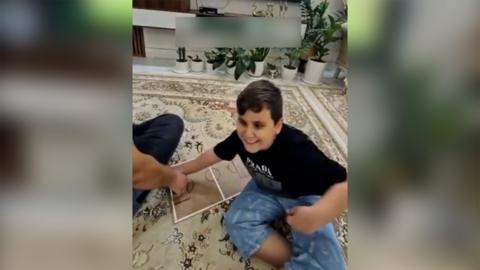 Boy smiling on carpet with a football tactics board in front of the football on TV