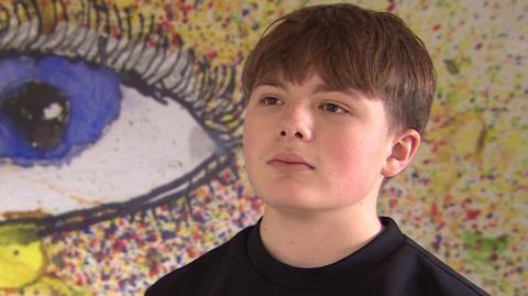Callum Thain has short brown hair and is wearing a black top. He is wearing a semi-serious expression.