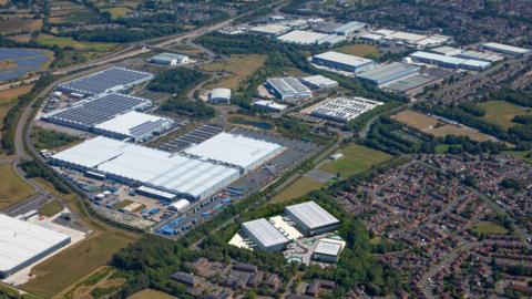 An overhead view of a vast industrial site, next to a housing estate, showing a view of several warehouses.