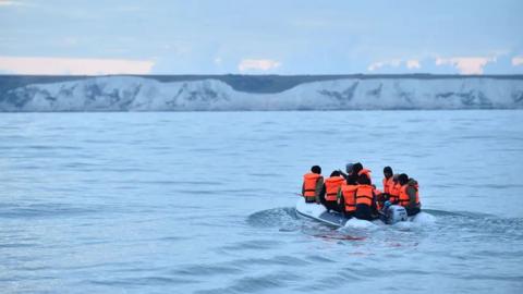 A group of people on an inflatable boat with the White Cliffs of Dover in the background.