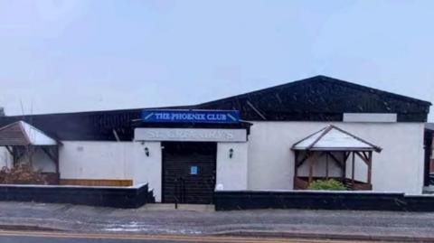 A low set white building with a sign that reads 'The Phoenix Club' and 'St Gregory's' as seen from a street. 