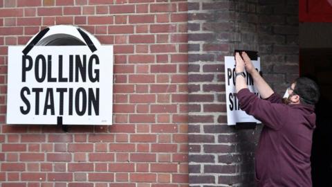 An election officer reattaches a polling notice at a polling station in southwest London