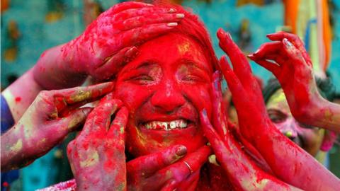 A woman reacts as devotees apply coloured powder on her face during celebrations for Holi outside a temple on the outskirts of Kolkata, India, 21 March 2019.