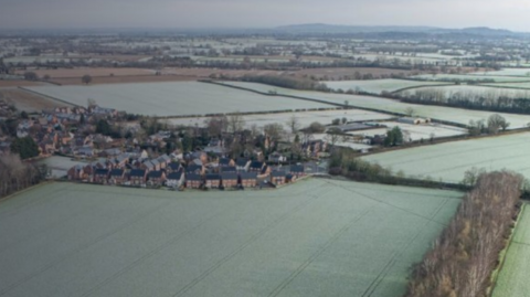 An aerial view of a small number of homes, surrounded by green fields