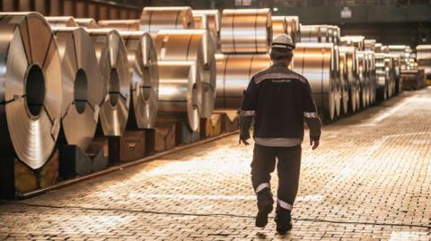 A worker walks past coils of finished steel at the Thyssenkrupp steel mill in Duisburg, Germany. Photo: 20 March 2025