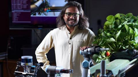 Dr Vishwanathan Mohan, who is wearing a white shirt, with his hand on the robot, which is next to an unpicked strawberry.