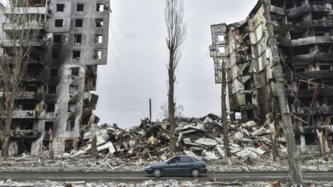 Image shows car driving among wreckage