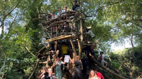 Children playing in a treehouse near a woodland