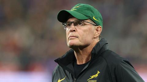 Rassie Erasmus wears a green cap and glasses and a dark top