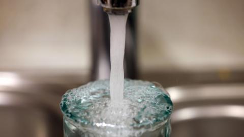 A tap of running water flowing into a glass which is full of water.