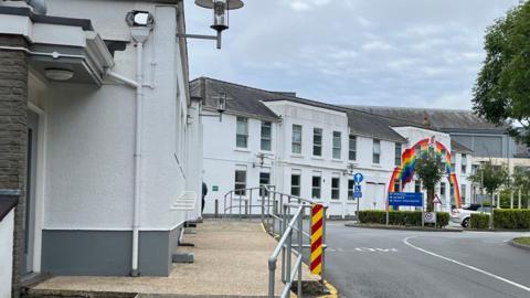 A ranbow painted on a white building with handrails along a pathway. 