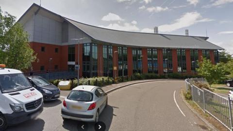 Loddon Valley Police Station - a red brick building that curves with the curve in the road. It has lots of windows. There are two cars and a van parked up to the right in the foreground.