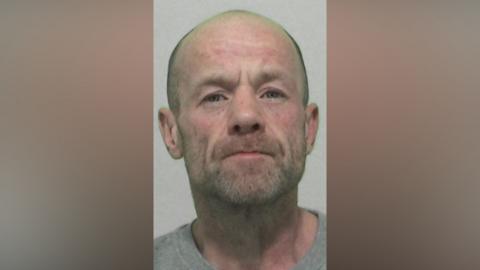 Mugshot of Thomas Brand. He has grey stubble and is bald.