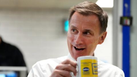 Jeremy Hunt looks up as he has a drink and biscuits with employees during a visit to a builders warehouse