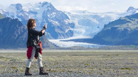 A photographer takes a picture of a landscape in Iceland