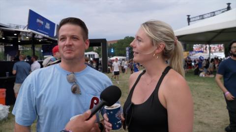 A man in a light blue T-Shirt and a woman in a black singlet speaks in to a microphone.