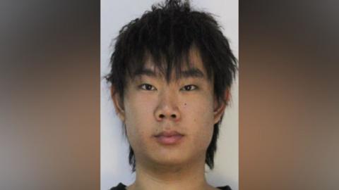 Mugshot of Li. He is clean shaven with neck-length, thick black hair.