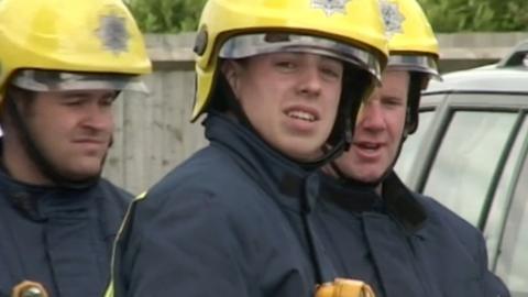 Martyn Sadler stands in firefighter kit wearing a yellow helmet with a visor and a dark blue coat