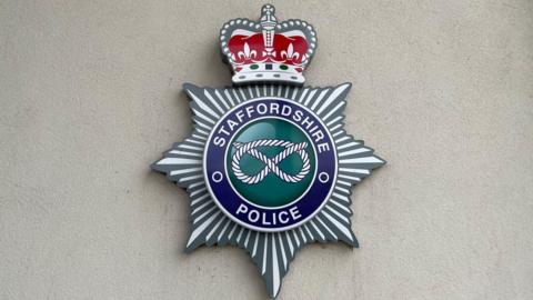 A large crest on a concrete wall, with the words Staffordshire Police, and an image of a knot in the middle
