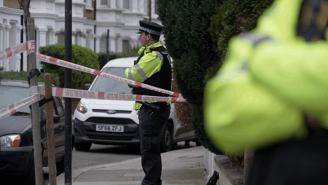 A police officer standing within a police cordon on Lena Gardens.