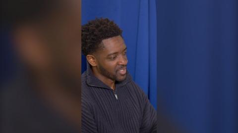 A man with short black hair wearing a blue jumper