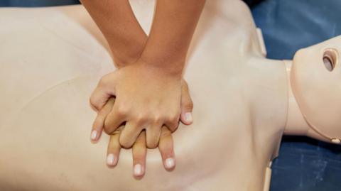 Cropped hands CPR First Aid training with CPR dummy in the classroom.