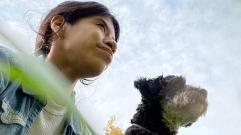 A girl sitting in the grass with her dog looking away from the camera