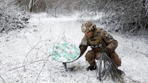 A soldier sets a Starlink dish down in a snowy field