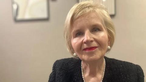 Donna Ockenden looking at the camera. She has short blonde hair and is wearing a black top with a string of pearls