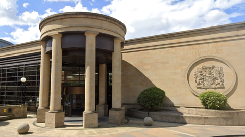 The outside of the High Court in Glasgow. a sandstone building with pillars at the entrance and the legal system insignia on the wall