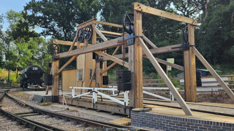 Wood framed bridge and lift over a railway track with steam train behind