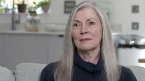 Carolyn Woods looking at the camera as she sits on a grey sofa Copyright