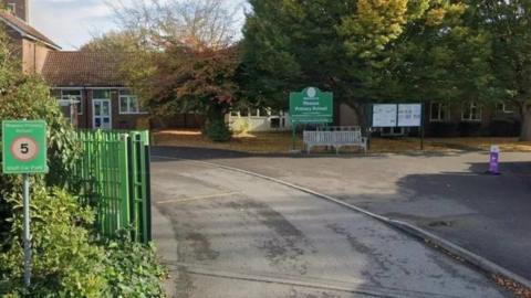 Green gates and signs along road leading to school building.