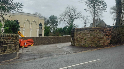 The stone entrance to the Issa brother's mosque with a white building behind it and an orange work fence