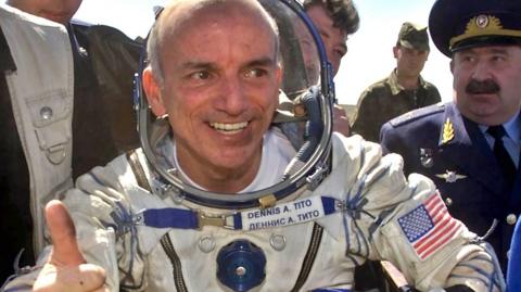 Dennis Tito in a space suit giving a thumb's up
