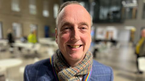 Liberal Democrat leader on Wiltshire Council Ian Thorn smiles at the camera in a blue suit jacket and woolly scarf.