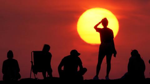 People silhouetted as they turn out to watch the sunrise at Cullercoats Bay, North Tyneside on July 19, 2022.